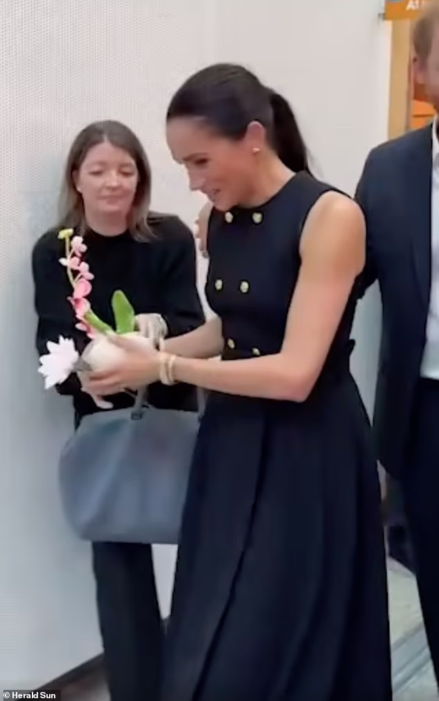 Proprio come un reale che lavora! Momento in cui Meghan consegna fiori al suo assistente durante la visita in stile reale all’ospedale pediatrico di Melbourne con Harry